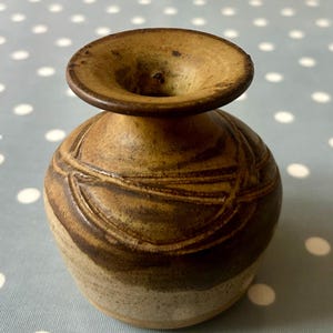 May include: A small, brown ceramic vase with a wide mouth and a narrow neck. The vase has a textured, swirling design.