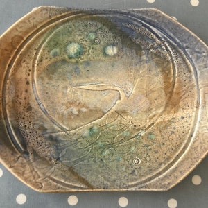 May include: A ceramic plate with a blue, green and brown glaze. The plate features a raised design of a bird in flight.
