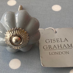 May include: A grey ceramic cabinet knob with a silver metal centre. The knob is shaped like a flower with five petals. The knob is labelled "GISELLA GRAHAM LONDON".