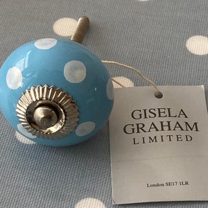 Könnte beinhalten: Ein hellblauer Keramik-Knopf mit weißen Punkten und einem silbernen Metallfuß. Der Knopf ist mit "Gisela Graham Limited, London SE17 1LR" beschriftet.