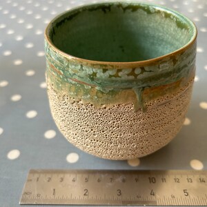 May include: A small, round ceramic planter with a textured, beige exterior and a green glaze on the top rim. The planter is approximately 4 inches in diameter.