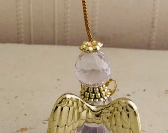 Op de afbeelding: Een helder glazen engel ornament met gouden vleugels en een gouden parelrand. Het ornament heeft een lus aan de bovenkant om op te hangen.