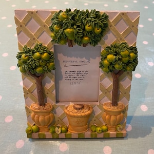 Puede incluir: Un marco de fotos blanco con un diseño de enrejado verde y amarillo. El marco presenta tres árboles esculpidos con hojas verdes y frutos amarillos. El marco tiene una abertura de 61 cm x 84 cm y una inscripción manuscrita que dice "Rejoiceful Singing. The children sing in for joy, the children sing in Spain; the organ with the organ man is singing in the rain."