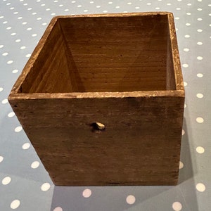 May include: A rustic wooden box with a single hole in the front. The box is made of natural wood and has a weathered, aged look.