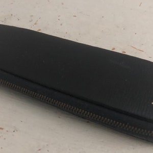 Op de afbeelding: Een zwarte etui met rits en de tekst "HITACHI" in gouden letters.