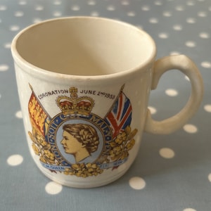 May include: White ceramic mug featuring a commemorative design for the coronation of Queen Elizabeth II on June 2nd, 1953. The design includes a portrait of the Queen, the royal crown, and the flags of Canada and the United Kingdom.