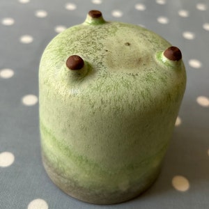 May include: A green ceramic planter with three brown feet. The planter has a mottled green glaze and a darker green band around the bottom.