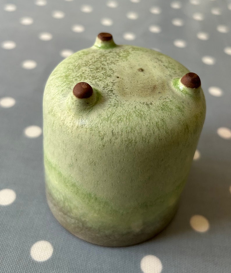 May include: A green ceramic planter with three brown feet. The planter has a mottled green glaze and a darker green band around the bottom.