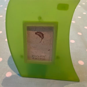 May include: A green picture frame with a curved edge and a small leaf design. The frame is 8 1/2 inches by 3 1/2 inches, or 6 cm by 9 cm.