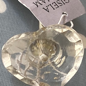 Puede incluir: Un pomo de armario de cristal transparente en forma de corazón con un tornillo de metal plateado. El pomo está hecho por Gisela Graham Limited.
