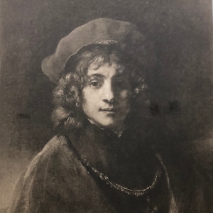 May include: A black and white portrait of a young person wearing a dark cap and a dark cloak. The person has curly hair and is looking directly at the viewer.