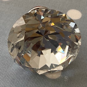 May include: A large, clear, faceted gemstone. The round gem is cut to maximise light refraction, displaying a spectrum of colours. The facets create a complex pattern of light and shadow. The gem's surface is highly reflective.