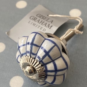 Puede incluir: Pomo de armario de cerámica blanca con un patrón de cuadros azul y blanco. El pomo tiene una base de metal plateado y un anillo decorativo de metal plateado alrededor de la parte superior. El pomo está unido a un tornillo de metal plateado. El pomo tiene una etiqueta adjunta que dice "Gisela Graham Limited".