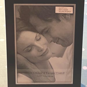 May include: A black picture frame with a silver mat and a black and white photo of a couple. The frame is 5x7 inches and 13x18 cm. The frame is hand polished and lacquer coated. The text on the frame reads "D16757-211 SIZE available- 2x3, 4x6, 5x7, 8x10"