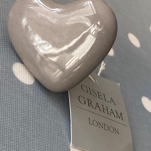 May include: A grey ceramic heart with a glossy finish. The heart has a tag attached to it that reads "Gisela Graham London".