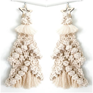May include: Two cream-colored macrame Christmas trees with wooden star ornaments hanging from the top. The trees are made with a crocheted design and have a fringe at the bottom.