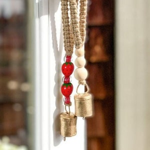 May include: A door handle with a hanging decoration made of natural jute rope, wooden beads, and red strawberry charms. The decoration also includes three small gold bells.