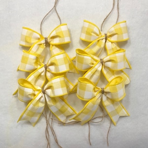 May include: Six yellow and white gingham bows with twine attached. The bows are arranged in a stack.