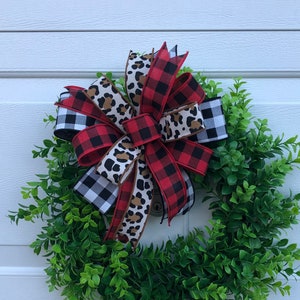 May include: A green wreath with a large bow made of red and black buffalo plaid ribbon, black and white checkered ribbon, and brown and tan leopard print ribbon.