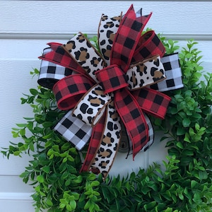 May include: A red, black, and white plaid bow with a leopard print ribbon, tied on a green wreath.