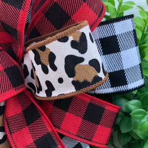May include: A close-up of a red and black buffalo plaid ribbon, a white and black buffalo plaid ribbon, and a brown and white leopard print ribbon. The ribbons are tied together in a bow.