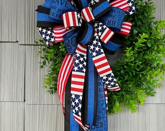 May include: A red, white, and blue ribbon wreath with a blue and black ribbon with the text "Peace Makers" and "Hero" on it. The wreath is decorated with a blue and black ribbon with a thin white stripe.
