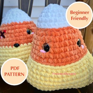 May include: Two handmade crochet candy corn plushies. Each plushie features a white top, orange center, and yellow base. They have black eyes, pink cheeks, and a stitched mouth. The image includes the text "Beginner Friendly" and "PDF PATTERN".