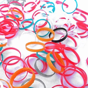 Peut inclure: Une collection d'anneaux en plastique de différentes tailles et couleurs, dont le rouge, l'orange, le jaune, le vert, le bleu, le blanc et le noir. Les anneaux sont disposés de manière aléatoire sur une surface blanche.