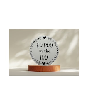 May include: White round sign with black text and a black heart design. The sign reads "No Poo in the Loo".
