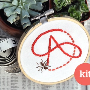 May include: A red embroidery kit featuring an ant carrying a red loop. The kit includes a hoop, fabric, and embroidery floss. The word "kit" is printed in white on a red circle.