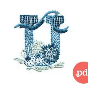 May include: Embroidered letter U with blue and white thread, featuring a floral design. The letter is stitched on white fabric.
