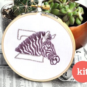 May include: A purple and white zebra embroidery kit in a wooden embroidery hoop. The hoop is 6 inches in diameter. The kit includes all the materials needed to complete the embroidery project.