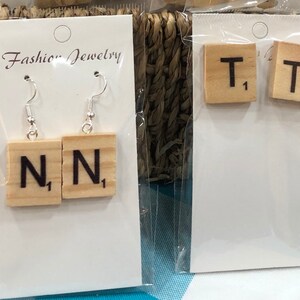 May include: Two pairs of earrings made from wooden Scrabble tiles. One pair features the letter "N" and the other pair features the letter "T".