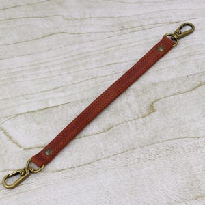May include: A brown leather strap with two gold metal clasps. The strap is about 10 inches long.