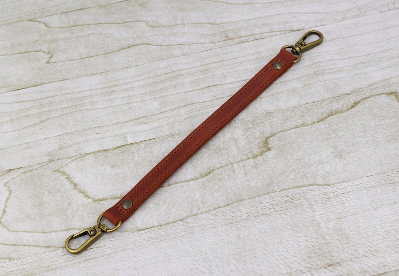 May include: A brown leather strap with two gold metal clasps. The strap is about 10 inches long.