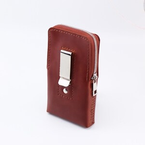 May include: A brown leather phone case with a zip closure and a metal clip. The case has a stitched design and a silver zip pull.
