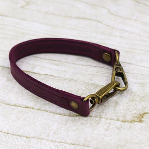 May include: A burgundy leather strap with a brass swivel hook. The strap is about 1 inch wide and has a stitched design.