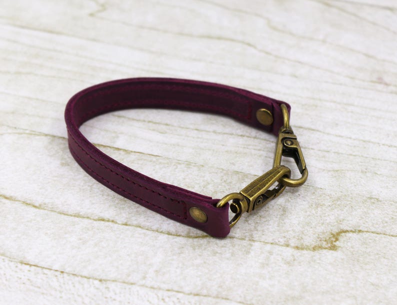 May include: A burgundy leather strap with a brass swivel hook. The strap is about 1 inch wide and has a stitched design.