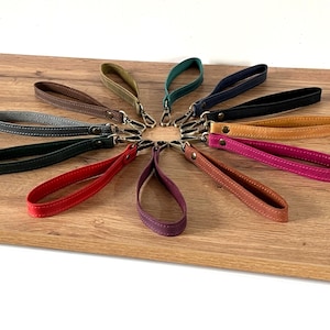 May include: A collection of ten wristlet straps arranged in a circular pattern. Each strap is made of a textured material in various colors including red, green, blue, black, brown, tan, pink, purple, and orange, featuring a metal clasp.