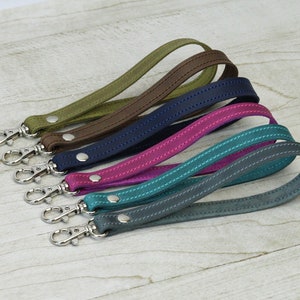 May include: Five leather keychains in different colors, including teal, pink, navy blue, brown, and green. Each keychain has a silver metal clasp.