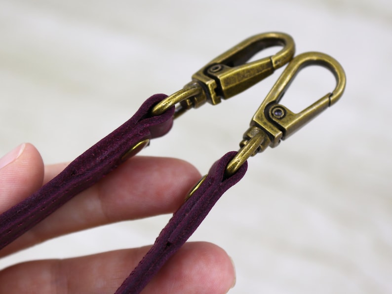 May include: Two burgundy leather straps with gold metal clasps. The straps are attached to the clasps with stitching.
