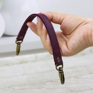 May include: Burgundy leather handbag strap with two gold metal clasps.