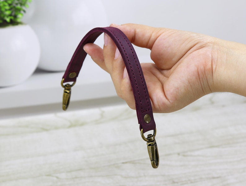 May include: Burgundy leather handbag strap with two gold metal clasps.