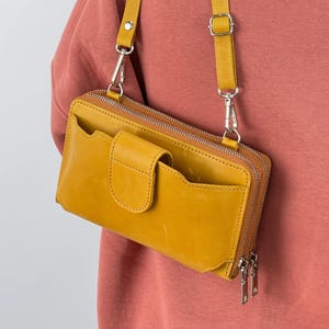 May include: Mustard yellow leather crossbody bag with a detachable shoulder strap. The bag has a front flap pocket, multiple compartments, and a zip closure. The hardware is silver-toned.
