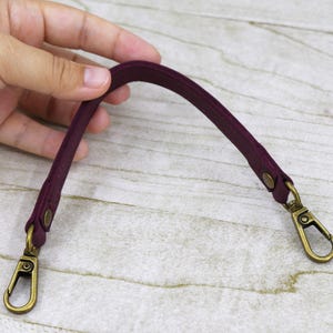 May include: A burgundy leather strap with two gold metal clasps. The strap is about 10 inches long.