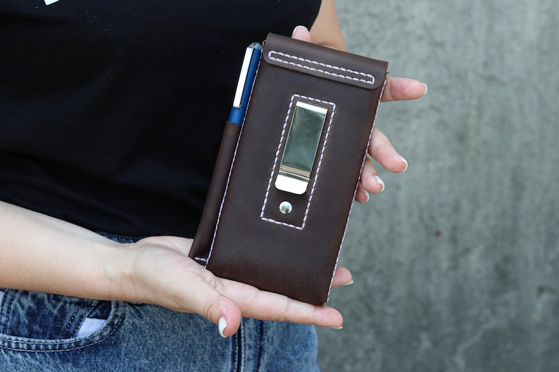 A brown leather phone case with a silver metal clip and a pen holder. The case has white stitching around the edges.