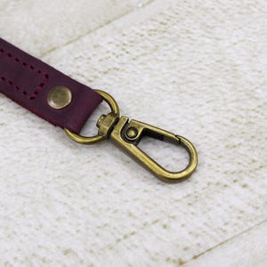 May include: A burgundy leather strap with a brass swivel clasp. The strap is stitched with a decorative pattern.