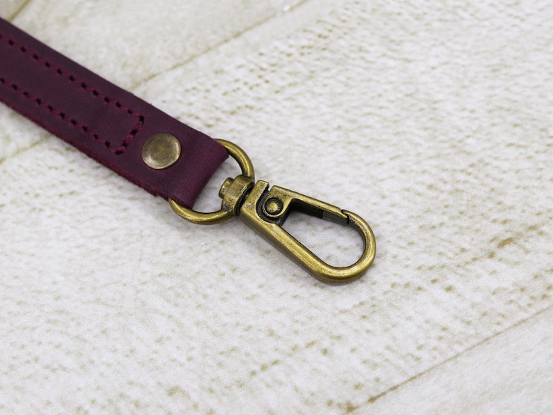 May include: A burgundy leather strap with a brass swivel clasp. The strap is stitched with a decorative pattern.