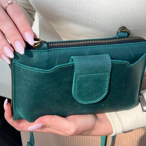 以下が含まれることがあります： アンティーク真鍮製の金具が付いた上部ファスナー開閉式のダークグリーンの長方形レザーショルダーバッグ。外側にスリップポケットがあり、中央のフラップはスナップボタンで留める仕様。ストラップを取り付けるためのサイドリングが付いています。