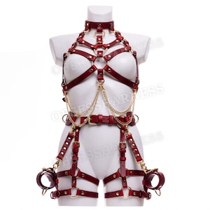 May include: A red leather harness with gold hardware and chains. The harness includes a choker, a chest piece, a belt, and thigh straps. The harness is designed with multiple straps and rings.